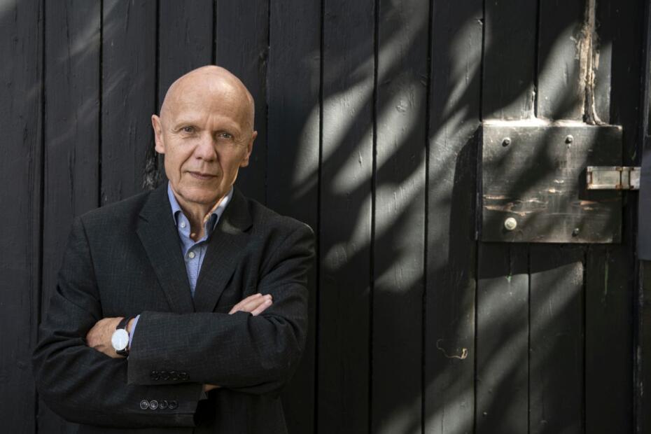 Georg Klein, Schriftsteller, in seinem Garten, steht mit verschränkten Armen vor einer Holztüre