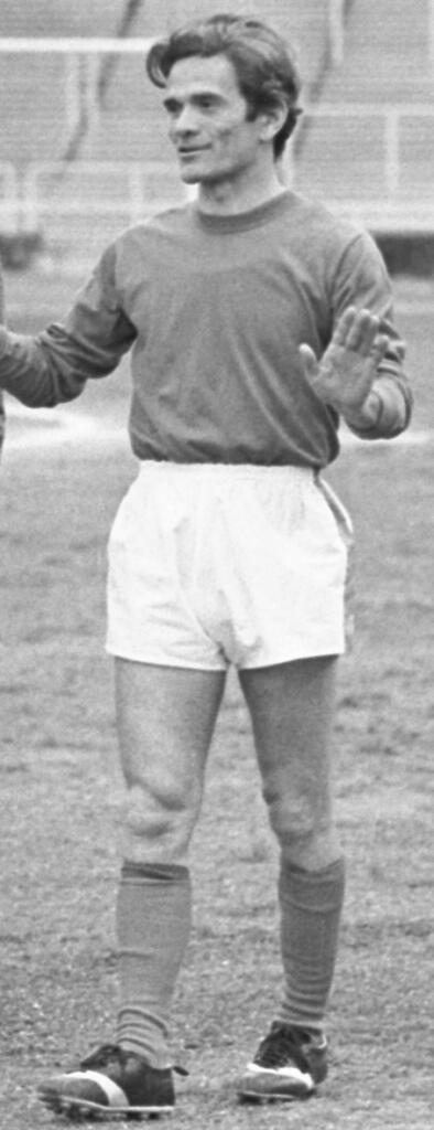 Schwarz-Weiß-Bild: Ein Fußballer steht da und macht mit den Händen eine beruhigende Geste.