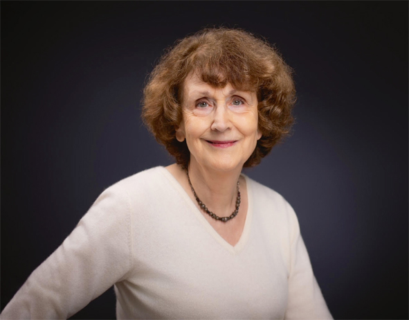 Frau Cecile Oumhani blickt in die Kamera. Oberkörperfoto. Sie hat braunes gelocktes Haar nd trägt einen weißes Oberteil mit V-Ausschnitt und eine Halskette.