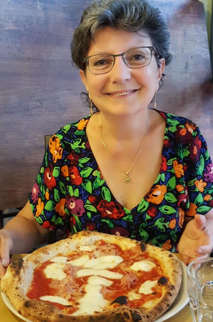 Eine Frau lächelt in die Kamera, vor ihr eine große Pizza Gorgonzola